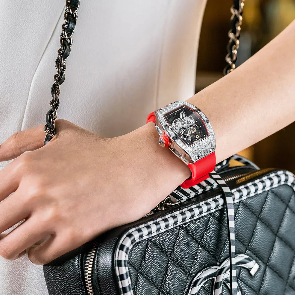 A woman's hand wearing a red-strapped luxury Geya watch with a diamond frame
